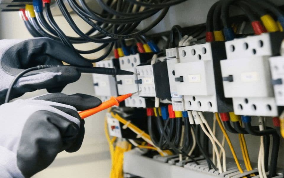 مهندس يفحص لوحة كهربائية بمقياس رقمي متعدد أثناء الصيانة الوقائية